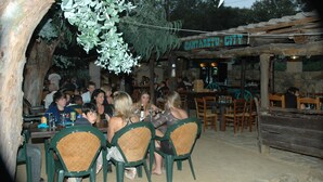 A rustic outdoor dining area with wooden tables and chairs, surrounded by greenery and a stone wall. - Algajola - New wooden air-conditioned chalet for 4/5, 1 km away from the beach (Algajola)
