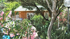 A wooden cabin with a tiled roof, surrounded by lush greenery and flowering plants. - Algajola - New wooden air-conditioned chalet for 4/5, 1 km away from the beach (Algajola)