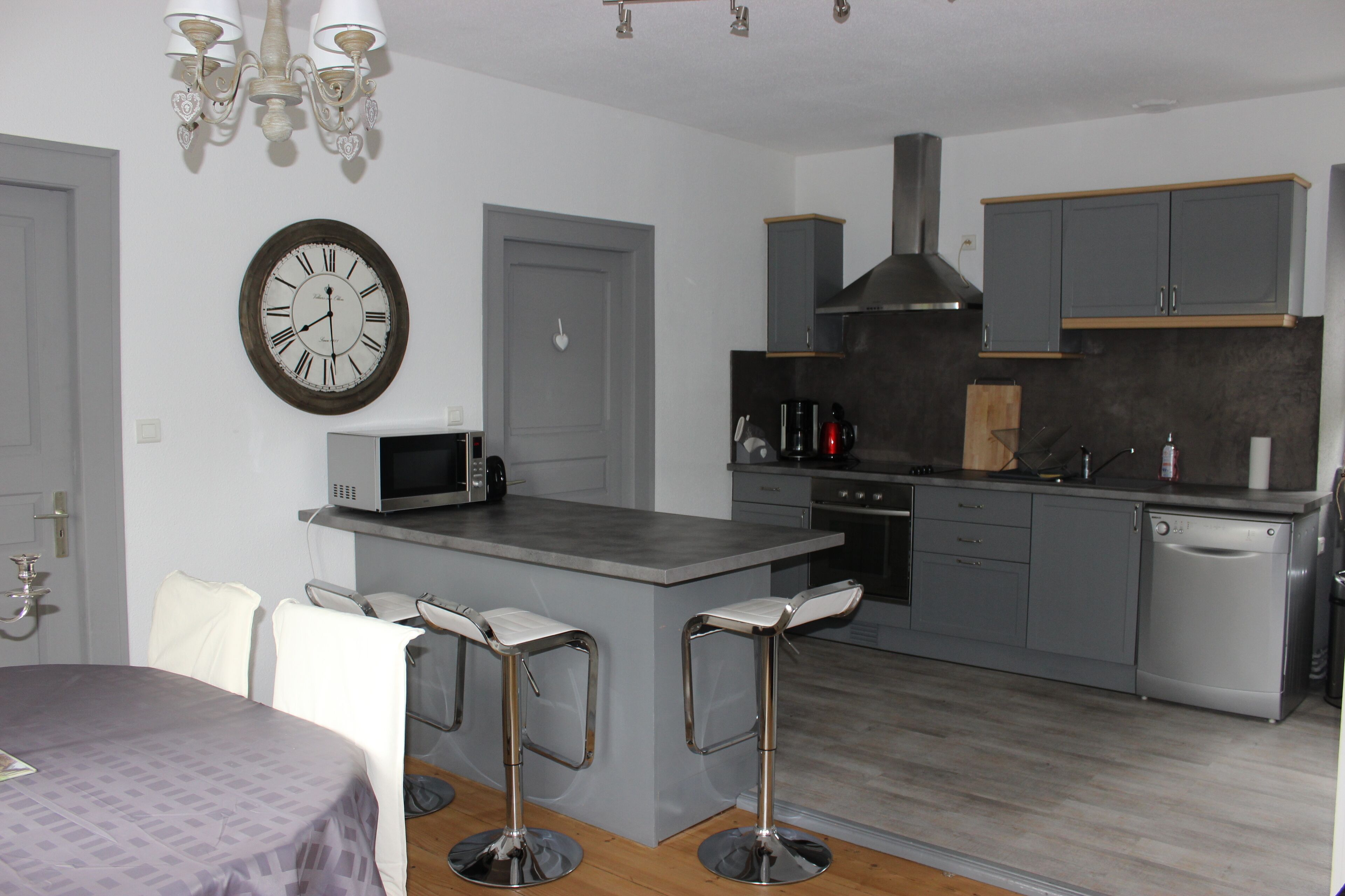 Une cuisine moderne avec des meubles gris, un îlot central doté de tabourets, un four à micro-ondes et une horloge murale.