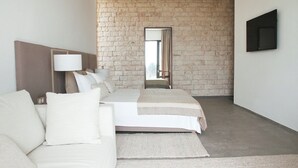 A modern bedroom with a stone wall, a bed, a sofa, a lamp, and a TV. - Luxurious villa with sea views in Essaouira (Essaouira)