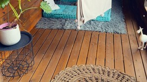 Una cama hamaca en una cabaña de madera con un banco acolchado azul, un tapete de crochet y una planta en maceta.