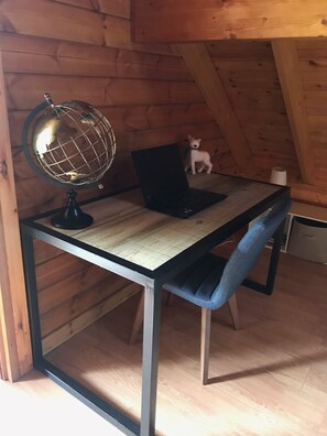 Ein Holztisch mit Globus, Laptop und Stofftier in einem Zimmer mit Holzwänden und schrägen Decken.