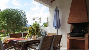 An outdoor dining area with a table and chairs, a blue umbrella, and a brick oven grill. - MINI VILLA in Corsica (Lecci)