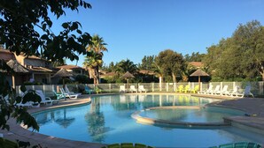 A swimming pool with multiple lounge chairs around it, surrounded by a white fence and palm trees. - MINI VILLA in Corsica (Lecci)