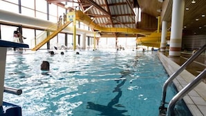 En indendørs swimmingpool med flere baner, en gul rutsjebane og en trappe op til en platform.