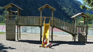 En legeplads med klatrestrukturer og en rutchebane, med et bjergrigt landskab i baggrunden.