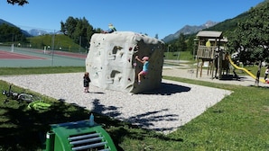 En klatrevæg i en park med en legeplads og en løbebane i baggrunden.