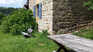 Ein rustikales Steinhaus mit einer Holzbank und einem Picknicktisch in einer grünen Wiese.