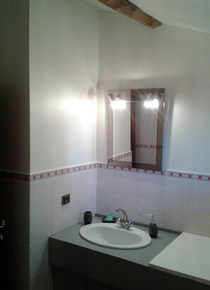 Une salle de bain avec un lavabo blanc, un miroir et un luminaire placé au-dessus du miroir.