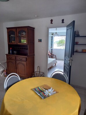 A dining area with a yellow table, a cabinet with glass doors, and a view of the outside through an open door.