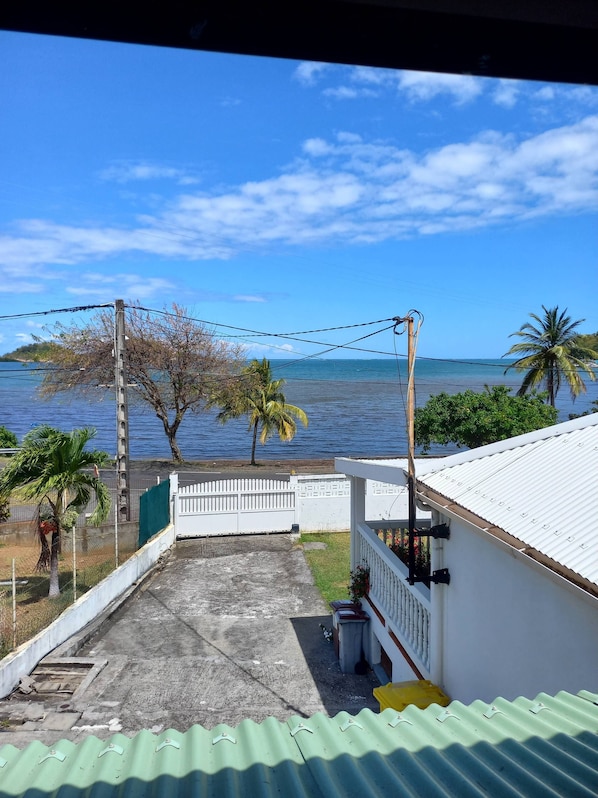 A view from a balcony overlooking a beach with palm trees and a white fence.
