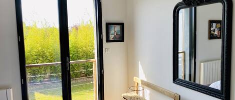 Un dormitorio con un ventanal grande, un banco de madera, un espejo y un cuadro enmarcado en la pared.