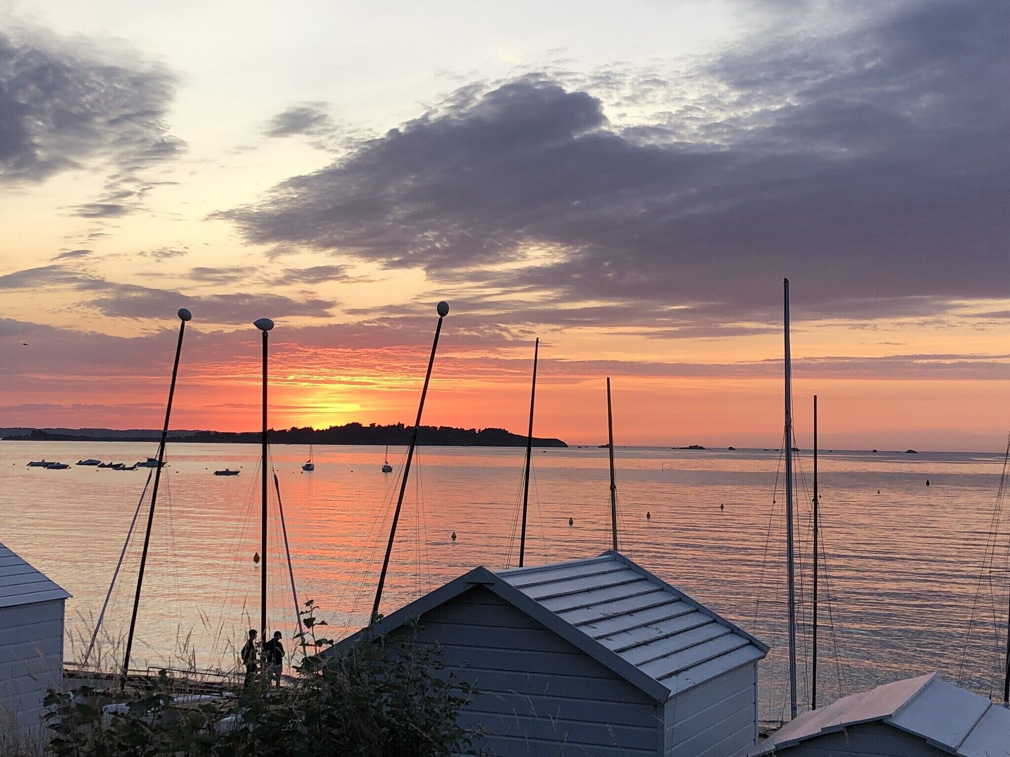 Um pôr do sol sobre um mar tranquilo, com barcos, um cais e um pequeno edifício.
