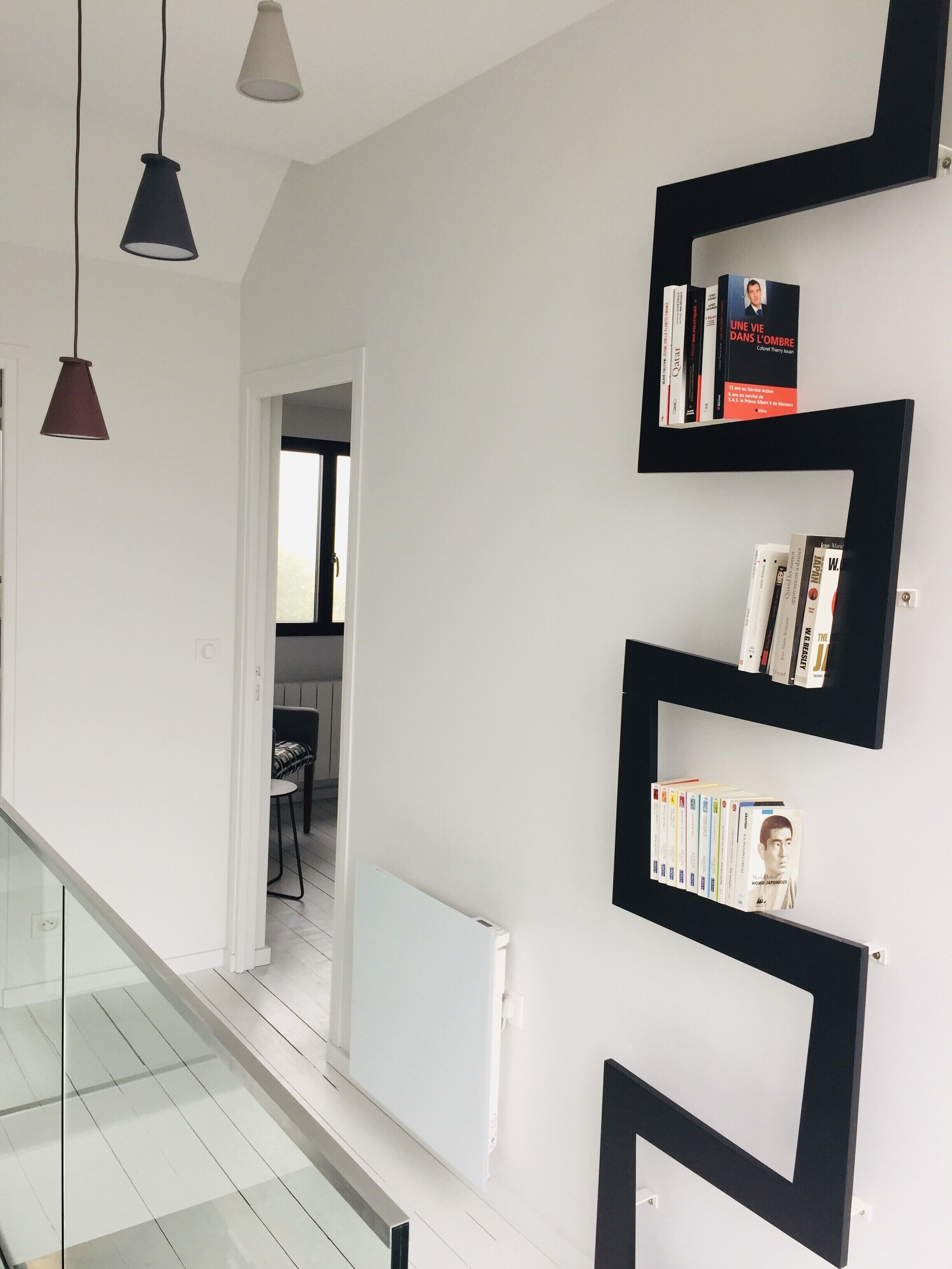 A modern interior with a staircase, black shelving units with books, and pendant lighting.