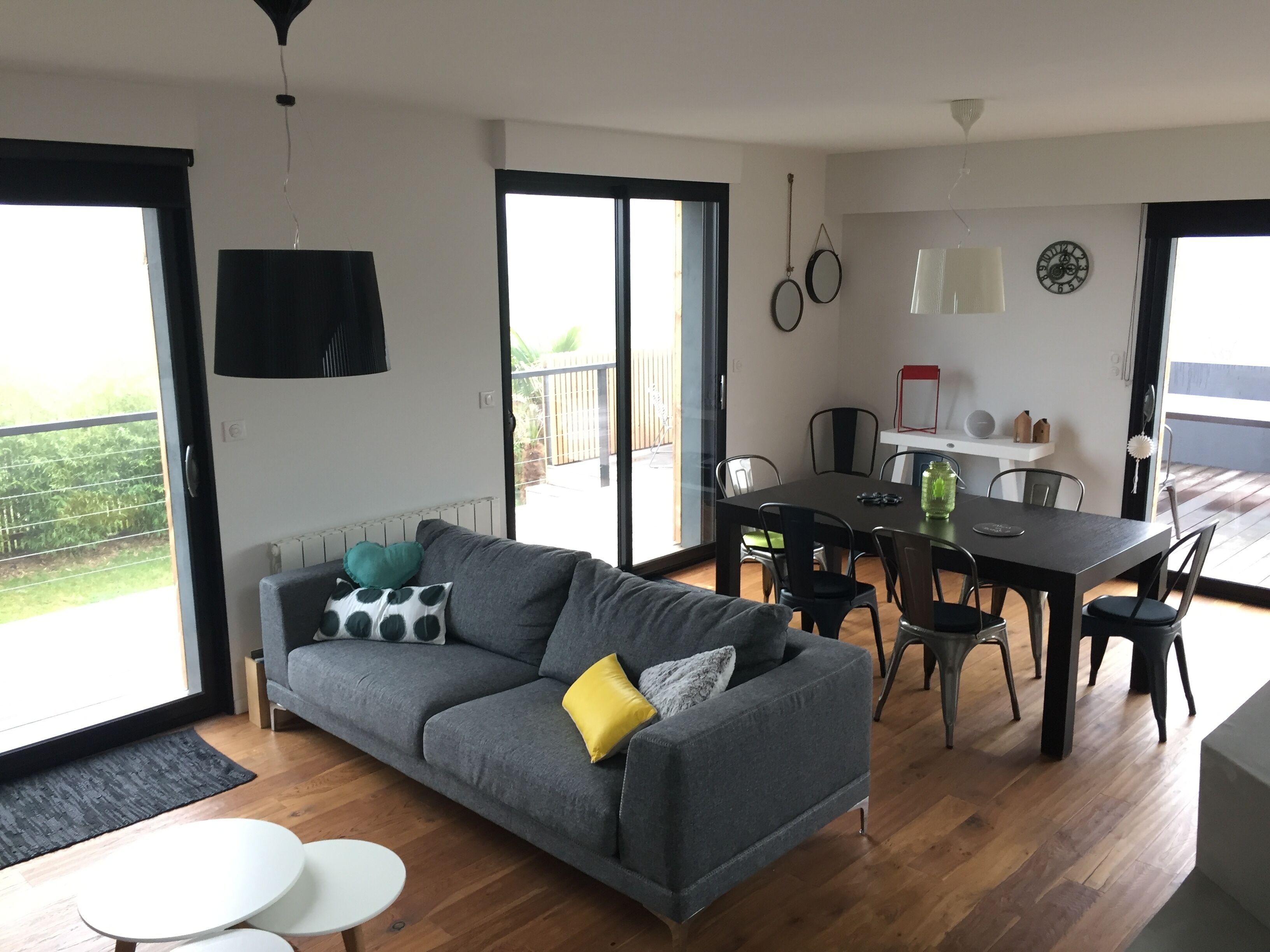 Una sala de estar moderna con un sofá gris, una mesa de comedor con sillas, y un balcón con vistas.