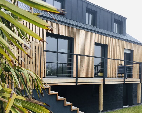 A modern two-story house with a wooden facade, large windows, and a balcony.