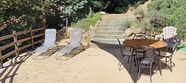A patio area with a wooden table and chairs, a wooden fence, and a set of stairs leading up.