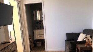 En moderne stue med trægulv, en sort sofa, et fjernsyn på et træskab og et lille bord med en lampe.