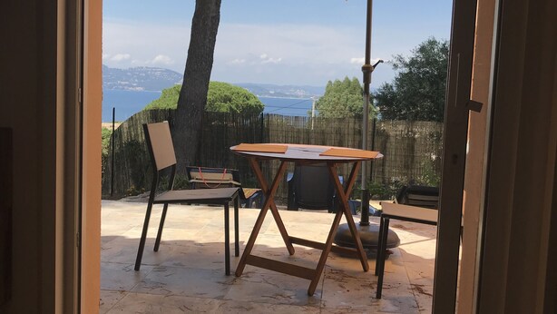 En terrasse med et bord og stole, en parasol og udsigt over havet.