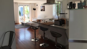 A modern kitchen with a white countertop, two bar stools, a coffee machine, and a large window.