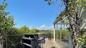 A wooden deck with a built-in barbecue area, a glass-enclosed patio, and a view of the surrounding greenery.