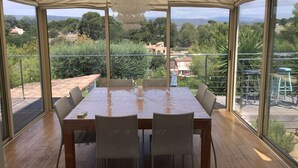 A covered outdoor dining area with a table and chairs, large windows offering a view of the surrounding landscape.