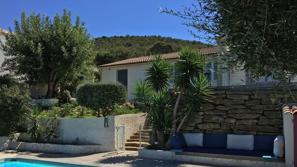 A swimming pool with a wooden deck, surrounded by greenery and a stone wall.