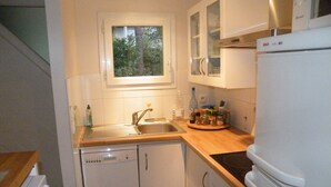 Una cucina compatta con elettrodomestici bianchi, una finestra sopra il lavello e vista sul verde.