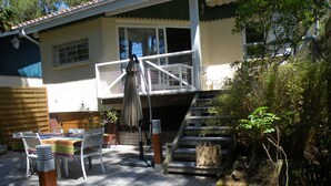 Un patio in legno con arredi da esterno, una zona salotto coperta e una scala che conduce a un balcone.