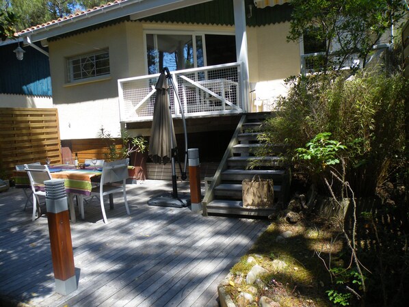 A wooden deck with outdoor furniture, a covered seating area, and a staircase leading to a balcony.