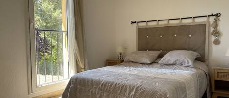 A bedroom with a bed, a nightstand, a window with curtains, and a view of trees outside.