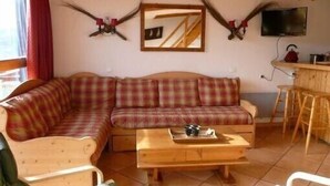 A cozy living room with a plaid sofa, wooden coffee table, and a TV mounted on the wall. - ARCS1800 very sunny 3 rooms 3 shower rooms balcony 50m Transarc and shops (Bourg-Saint-Maurice)