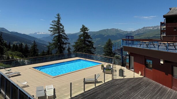 A swimming pool with a view of mountains, a wooden deck, and a red building. - ARCS1800 very sunny 3 rooms 3 shower rooms balcony 50m Transarc and shops (Bourg-Saint-Maurice)