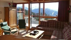 A cozy living room with a sofa, chairs, and a table. Large windows offer a view of mountains. - ARCS1800 very sunny 3 rooms 3 shower rooms balcony 50m Transarc and shops (Bourg-Saint-Maurice)