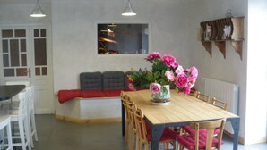 Un coin repas avec une table en bois, des chaises, un banc avec des coussins et un vase de fleurs.