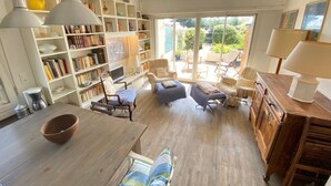 Un salon spacieux avec une grande bibliothèque, des sièges confortables, une table à manger en bois et une vue sur le jardin grâce à de grandes portes coulissantes.