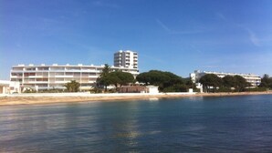 Un hôtel situé sur la côte, avec plusieurs étages, une plage de sable en premier plan et un ciel bleu dégagé.