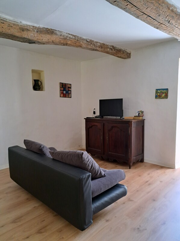 A room with a dark sofa, a wooden cabinet, a television, and a small painting on the wall. - Mimosa on a hillside, gite 4/6 pers, 2 suites (Thoiras)