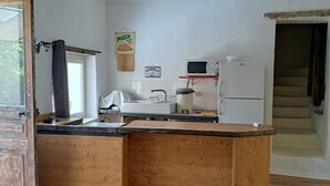 A kitchen with a wooden island, a microwave, and a refrigerator. There is a window with a curtain, and a sign that says "Pizza by the Office".