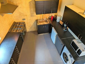 Cocina compacta con estufa a gas, lavamanos, lavadora y cafetera.