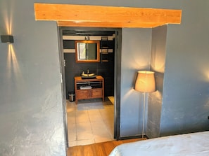 Un estrecho pasillo que conduce a un baño con un banco de madera, un espejo y una lámpara de pie.