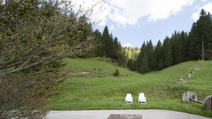 Une table de pique-nique se trouve dans un espace herbeux, avec deux chaises blanches et une roue en pierre à proximité.
