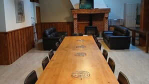 Une longue table à manger en bois, entourée de chaises, une cheminée en briques et un téléviseur fixé à une poutre en bois.