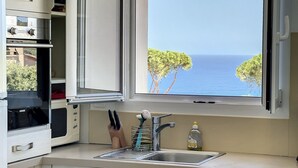 Uma cozinha com vista para o mar, uma pia e uma janela com persianas abertas.