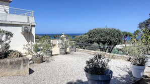 Jardim no terraço com plantas em vasos, vista para o mar e um edifício com fachada branca.