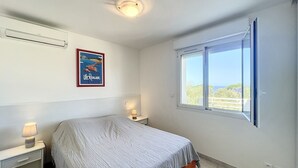 Um quarto com cama, mesa de cabeceira, luminária, pôster e janela com vista.