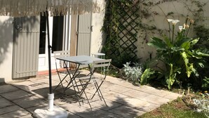 A patio with a table and chairs, a white umbrella, and a white wall with climbing plants. - Gloria's house ...   (Saint-Rémy-De-Provence)