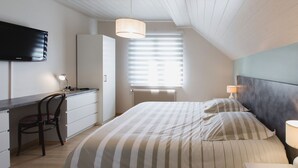 Une chambre à coucher avec un lit, un bureau, une chaise, un téléviseur et une fenêtre avec des stores.