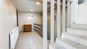 Un couloir avec un radiateur, une armoire en bois et un escalier recouvert de carreaux blancs.