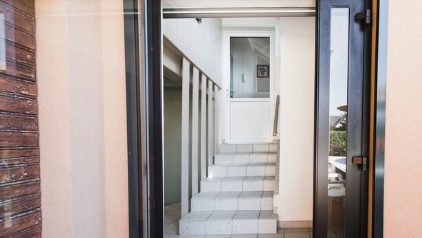 Un escalier menant à l’étage supérieur, avec une porte sur la droite et une rambarde sur la gauche.